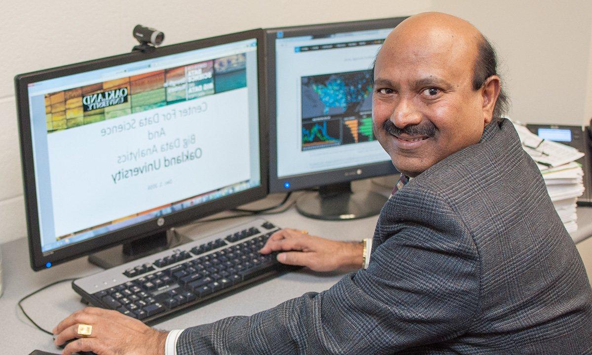 Man working on computer, turns from desk toward camera.